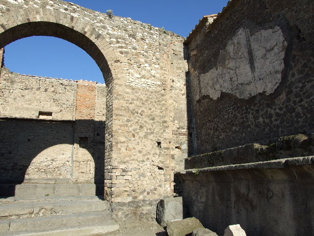 VII.8.1 NW corner Arch, showing arched niche on the south side of the rear wall at the back of the niche altar on the north street side