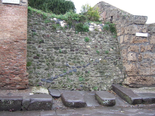 III.2.1 Pompeii. December 2007. Front wall on west side of entrance on Via dell’Abbondanza.   The wall on this side of the entrance was destroyed when a bomb landed in the atrium on 19th September 1943.
All of the painted graffiti, electoral recommendations and an announcement of games in the amphitheatre were lost. The wall on the east side was devastated by another bomb landing to the south-east of the house in the Via dell’Abbondanza. A small portion of the writings on the east side were saved, restored and can still be read today. See III.2.1 pt 10.   See Garcia y Garcia, L., 2006. Danni di guerra a Pompei. Rome: L’Erma di Bretschneider. (p.51-53, incl.photos).  
According to Della Corte, some of the inscriptions on the west side of the doorway to confirm the house as belonging to Trebius Valens, were –
Valens  fac,  et  ille  te  fecit      [CIL IV 7618]
Trebi,  surge, fac   [CIL IV 7619]
Trebi  Valens,  dormis   [CIL IV 7614]
Trebius  soda(lis)  facit,  Trebius  rog(at)    [CIL IV 7617]
See Della Corte, M., 1965.  Case ed Abitanti di Pompei. Napoli: Fausto Fiorentino. (p.345)
According to Epigraphik-Datenbank Clauss/Slaby (See www.manfredclauss.de), these read as -
Popidium  L(uci)  f(ilium)  Ampliatum  aed(ilem)
Valens  fac(it)  et  ille  te fecit  Infan..(tio)      [CIL IV 7618]
Trebi  surge  fac(it)
aed(ilem)  Lollium  Fuscum
adulescentem  probum       [CIL IV 7619]
L(ucium)  Popidium  Secundum  f(ilium)  aed(ilem)  v(irum)  b(onum)  o(ro)  v(os)  f(aciatis)
Trebi  Valens  dormis     [CIL IV 7614]
Caecilium  IIvir(um)
/
Trebius  soda(lis)  facit  Trebius  rog(at)    [CIL IV 7617]
According to Varone and Stefani, also lost from this wall were the following CIL IV 7611, 7612, 7613, 7616 and 7991.
None of these have been conserved.  See Varone, A. and Stefani, G., 2009. Titulorum Pictorum Pompeianorum, Rome: L’erma di Bretschneider, (p.233-5, with photo of the wall in c.1918)
CIL IV 7991 was an advertisement for the gladiatorial games in the amphitheatre, and according to Epigraphik-Datenbank Clauss/Slaby (See www.manfredclauss.de), read as  –
 Cn(aei) Allei Nigidi / Mai quinq(uennalis) sine impensa publica glad(iatorum) par(ia) XX et eorum supp(ositicii) pugn(abunt) Pompeis // Gavellius Tigillo / et Clodio sal(utem) / Telephe summa rudis / instrumentum muneris / u(bique) v(ale) / Diadumeno et Pyladioni fe(liciter)
According to Cooley, this advertisement was painted in black and red and was dated around AD 55/56 or later.   It translates as –
20 pairs of gladiators of Gnaeus Alleius Nigidius Maius, quinquennial, and their substitutes will fight without any public expense at Pompeii.
See Cooley, A. and M.G.L., 2004. Pompeii : A Sourcebook. London : Routledge. (p.53)
