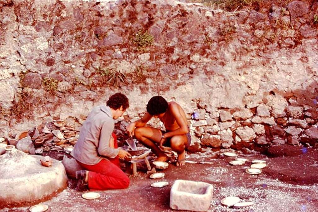 III.7 Pompeii. 1976. Two of Wilhelminas helpers, Raffaele and Renato, kneeling down and pretending to cook on the brazier. Photo by Stanley A. Jashemski.   
Source: The Wilhelmina and Stanley A. Jashemski archive in the University of Maryland Library, Special Collections (See collection page) and made available under the Creative Commons Attribution-Non Commercial License v.4. See Licence and use details. J76f0478
