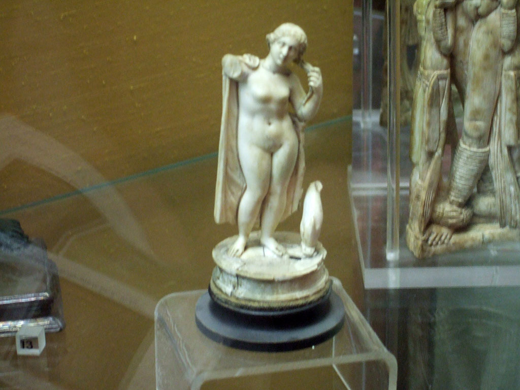 Ivory statuette of Venus Anadyomene with dolphin found in V.1.18 Pompeii.  
Now in Naples Archaeological Museum.  Inventory number 110924.
According to the note in Boyce, two statuettes were found in the tablinum “g”.
One was this ivory figurine of Venus with a mantle over her shoulders and a dolphin at her feet.
Also found was a bronze figure of Jupiter. He held a thunderbolt in his left hand, and a silver sceptre in his right, at his feet stood an eagle.
See Boyce G. K., 1937. Corpus of the Lararia of Pompeii. Rome: MAAR 14. (p.32, note 2) 
