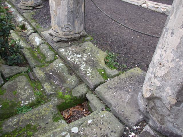 VI.6.1 Pompeii. September 2004. Peristyle, looking east along the south portico. According to Jashemski, the peristyle garden was enclosed on all four sides by an elegant portico. This portico was supported by sixteen stuccoed columns, painted yellow below, white and fluted above.
A cistern puteal stood between the first two columns at the south end of each of the long sides of the portico. Only the puteal on the west side (left in photo above) is preserved.


