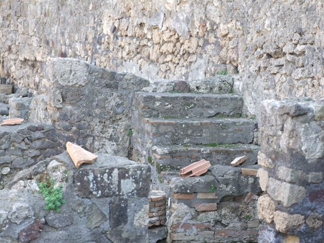VI.7.7 Pompeii. December 2005. Kitchen, with bench and hearth against the west wall. According to Boyce, on the north wall of the kitchen was a lararium painting. Only a fragment was preserved, painted on a white background. In the centre was the Genius with a cornucopia and patera standing before a burning altar. Behind him was a camillus, above and behind the altar was the figure of the tibicen. On either side of this group stood the Lares in yellow tunic and green pallium. Beyond the Lar on the left was a small popa pushing a hog towards the right. The corresponding figure on the right of the right Lar was missing, as was the whole outer section of the plaster on this side. In the lower zone was the customary altar with the two serpents. See Boyce G. K., 1937. Corpus of the Lararia of Pompeii. Rome: MAAR 14. (p.47, no.163)
Boyce added a note that said Helbig (58) wrongly assigned this shrine to VI.7.9. See Helbig, W., 1868. Wandgemälde der vom Vesuv verschütteten Städte Campaniens. Leipzig: Breitkopf und Härtel. (58)
