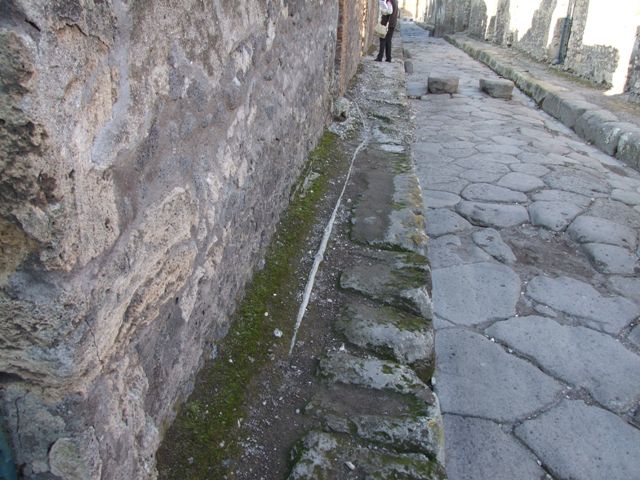 Lead pipe in pavement between VI.15.3 and VI.15.44 on Vico dei Vettii.  The pipe goes through the wall of VI.15.4.