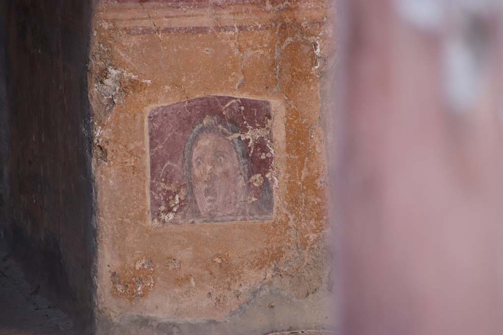 VI.16.15 Pompeii. September 2021. 
Atrium B, wall painting of face or mask between doorway to room E and room D at base of pilaster. Photo courtesy of Klaus Heese.
