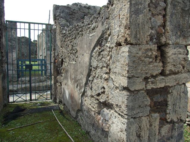 VI.16.27 Pompeii. March 2009. Room 16, recess in south wall of atrium.
According to Boyce, the doorway that led from the atrium to the peristyle was walled up, leaving a shallow recess in the south wall.
Within this recess, in the upper left corner, a white panel was marked off by green stripes on both sides. The figure of Jupiter was painted on the panel. He was seated upon a throne, leaning his forehead against his left hand, through the bend of this arm passed a long sceptre.
The lower end of the sceptre rested on the ground., in his right hand he held the thunderbolt. His feet were placed on a footstool and to its left stood an eagle. In the wall below the panel were embedded two broken tiles, one horizontal, the second perpendicular to the first at its west end. The wall space between the painting of Jupiter and the two tiles was decorated with plants painted on a yellow background. The horizontal tile may have served as a shelf for offerings, but the purpose of the two tiles was not clear. Found near the shrine was a terracotta votive altar. Not. Scavi, 1908, 184.  See Boyce G. K., 1937. Corpus of the Lararia of Pompeii. Rome: MAAR 14. (p.59, no.226)

