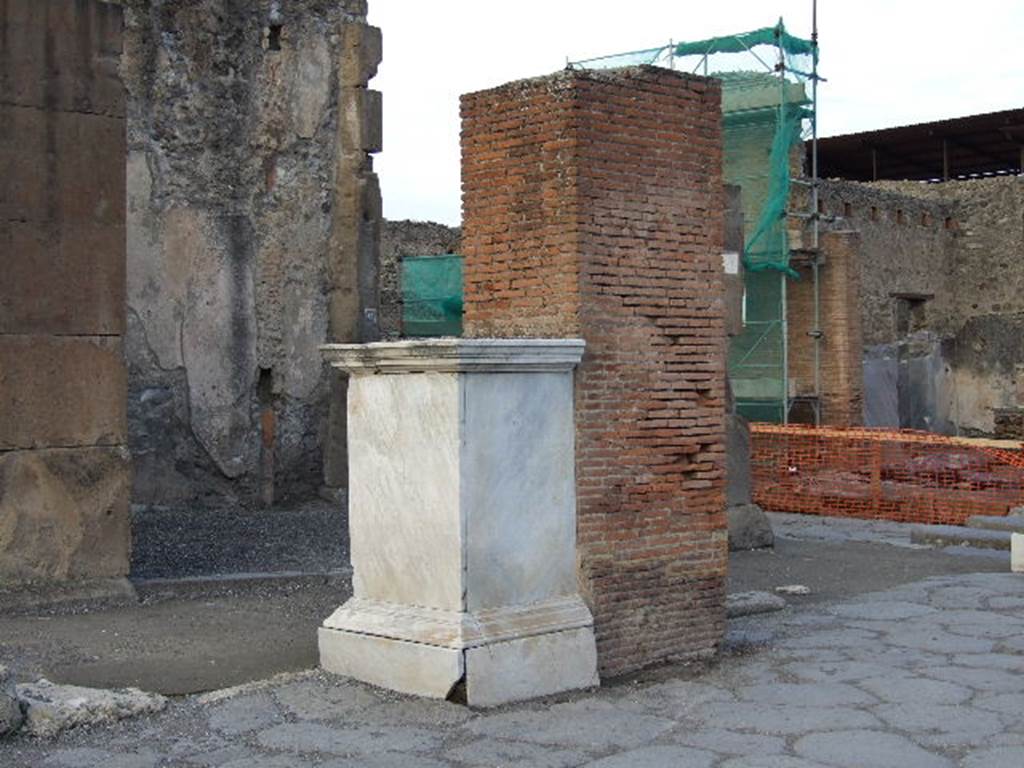 VII.1.12 in background behind pedestal which was the base of a statue of M. Holconius Rufus.  December 2006. The statue is now in Naples Archaeological Museum.  The brick pillar behind it was one of four which supported an arch over Via dell Abbondanza.
