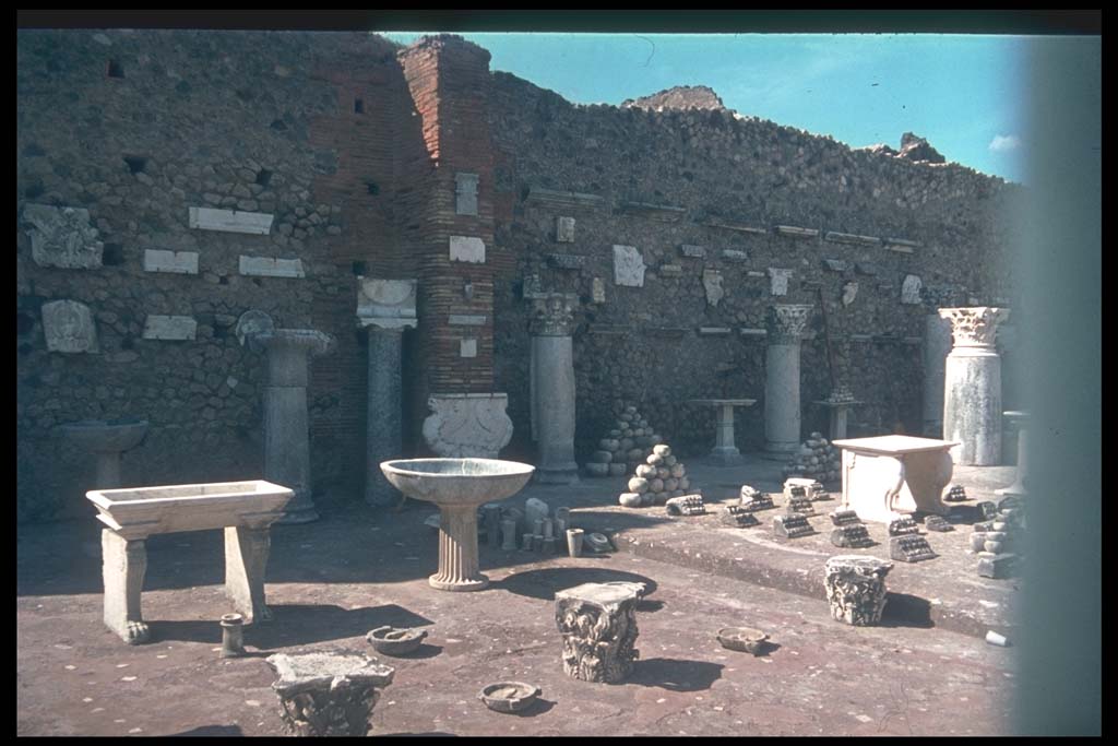 VII.7.29 Pompeii. Items on display and in storage.
Photographed 1970-79 by Günther Einhorn, picture courtesy of his son Ralf Einhorn.
According to Garcia y Garcia, it was Maiuri that restored the pilasters of this building and formed it into a display area.
Mostly these items on display are clay amphorae and domestic items from the houses, shops and workshops.
For the most part without provenance and classified only by type and form.
The bombing of 13th September 1943 caused the demolition of the south perimeter and part of the west wall
At least two of the seven pilasters of the entrance doorways were also demolished.
In 1946 Maiuri again restored the pilasters and roof.
See Garcia y Garcia, L., 2006. Danni di guerra a Pompei. Rome: L’Erma di Bretschneider. (p.116-7)
