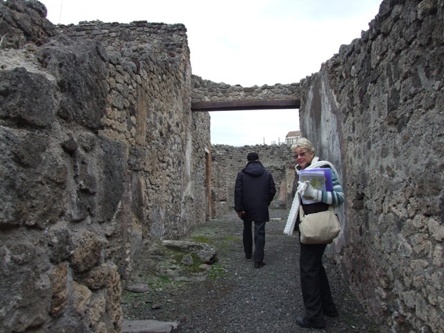 IX.1.7 Pompeii. December 2007. Lararium on south wall of atrium.
According to Boyce,there was a heavy masonry ledge above the panel painted to represent a block of red and yellow variegated marble, bordered in red. It was supported by twin scrolls and ornamented with several bands of stucco relief. On the masonry ledge were the bases of four delicate half-columns, two on each side of an arched niche.
A heavy gable roof used to project from the wall. Within the niche a polychrome stucco cornice runs around the middle of the walls, dividing them into sections, the upper one painted red, the lower one painted blue. On the blue background of the lower section are human figures in stucco relief – now poorly preserved. The arched ceiling is fitted with a shell of stucco. Around the curve of the arch on the wall outside runs another stucco cornice.
See Boyce G. K., 1937. Corpus of the Lararia of Pompeii. Rome: MAAR 14. (p.79, and Pl.6,1).