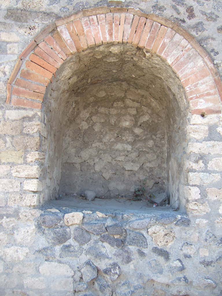Pompeii II.4.7a. September 2005. Street shrine at east end of II.4 on Via dell’Abbondanza.
Compital aedicula shrine.
When excavated in 1912, the following description was given in the Notizie degli Scavi:
Opening on to the public street pavement was an important sacellum with an arched niche 1.22m tall, 1.06m wide and 1.08m deep. 
It was ornamented above with a beautiful cornice in stucco plaster. 
The niche was a small temple in which were venerated the Penates or the protecting divinities in Pompeii. 
Two large holes with splinters of wood still attached were found in the floor of the shrine.
It was thought these were to anchor the figures of the Lares Compitales or were bases for them to stand on.
The statues had vanished, perhaps taken by ancient robbers who had cut a hole through the upper left corner of the shrine.
This damaged the decorative cornice and stucco relief on the façade.

