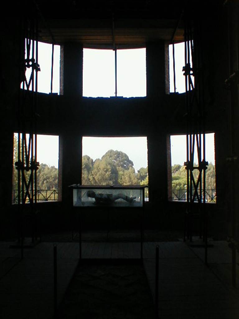 VII.16.17-22 Pompeii. September 2004. Looking west towards curved apse with six windows, in oecus.
A plaster cast of victim 48, is on display in the case.

