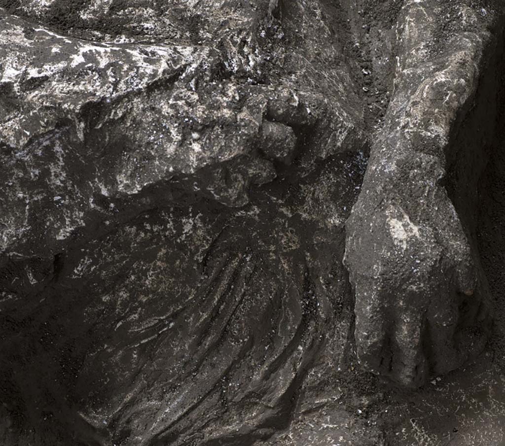 November 2020. Victim92. Detail of tunic and hands.
He wore a short tunic, of which the imprint of the drapery is clearly visible on the lower part of the belly, with thick rich folds and traces of heavy fabric, of a consistency which suggests that it was made of wool fibres. 

Novembre 2020. Vittima 92, dettaglio di tunica e mani.
Indossava una tunica corta, di cui è ben visibile l’impronta del panneggio sulla parte bassa del ventre, con ricche e spesse pieghe, la cui consistenza assieme alle tracce di tessuto pesante, fanno ipotizzare che si trattasse di fibre di lana. 

Photograph © Parco Archeologico di Pompei.

