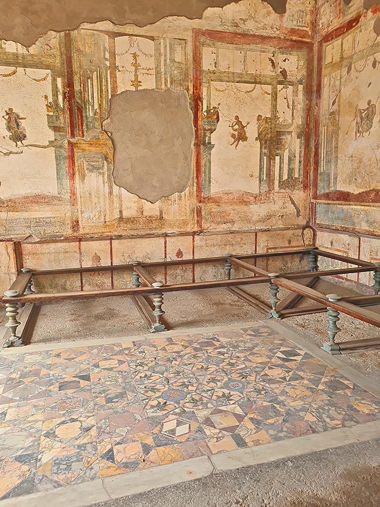 I.7.11 Pompeii. September 2024. 
Central painting removed from west wall of triclinium. Photo courtesy of Giuseppe Ciaramella.
According to PPM –
“I cuniculari hanno forato il quadro centrale, i cui frammenti raccolti dopo lo scavo sono stati ricomposti su un supporto moderno visibile nella parete E.”
(The tunnellers have pierced the central painting, the fragments of which collected after the excavation have been recomposed on a modern support visible in the east wall.)
See Carratelli, G. P., 1990-2003. Pompei: Pitture e Mosaici. I. Roma: Istituto della enciclopedia italiana, (p. 686, no. 114).
