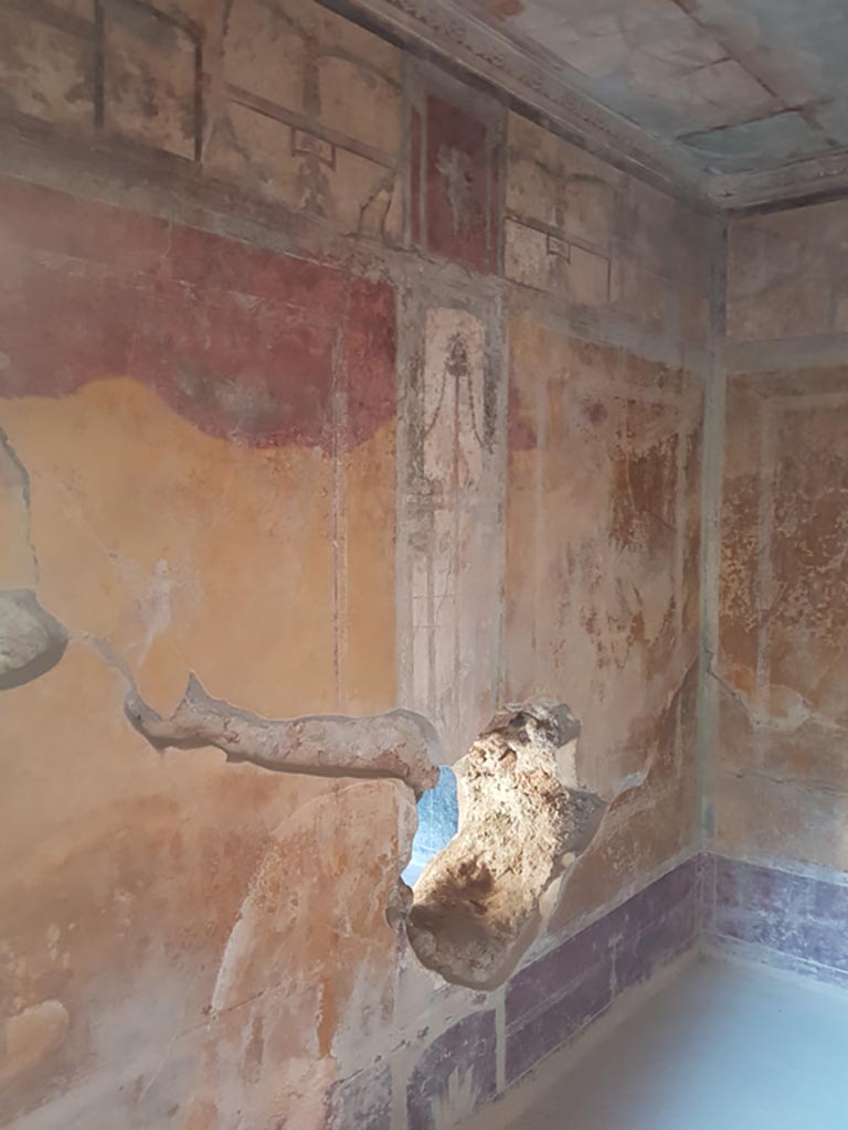 I.10.11 Pompeii. October 2022. Room 13, looking east along north wall.
The fact that the red painted walls have changed to yellow/orange is taken as a sign of intense heat/burning. 
Photo courtesy of Klaus Heese. 

