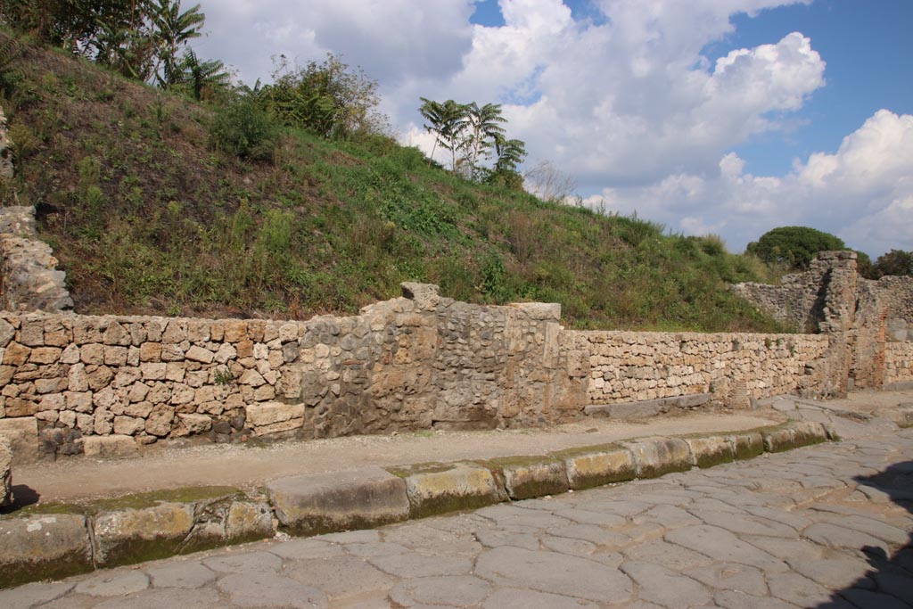 III.7.2 Pompeii. October 2022. Continuation from previous photo, see III.7.1.
Looking east along front façade towards entrance doorway to shop with grey lava doorway threshold, centre right, next to ramped entrance to III.7.3, on right. 
Photo courtesy of Klaus Heese
