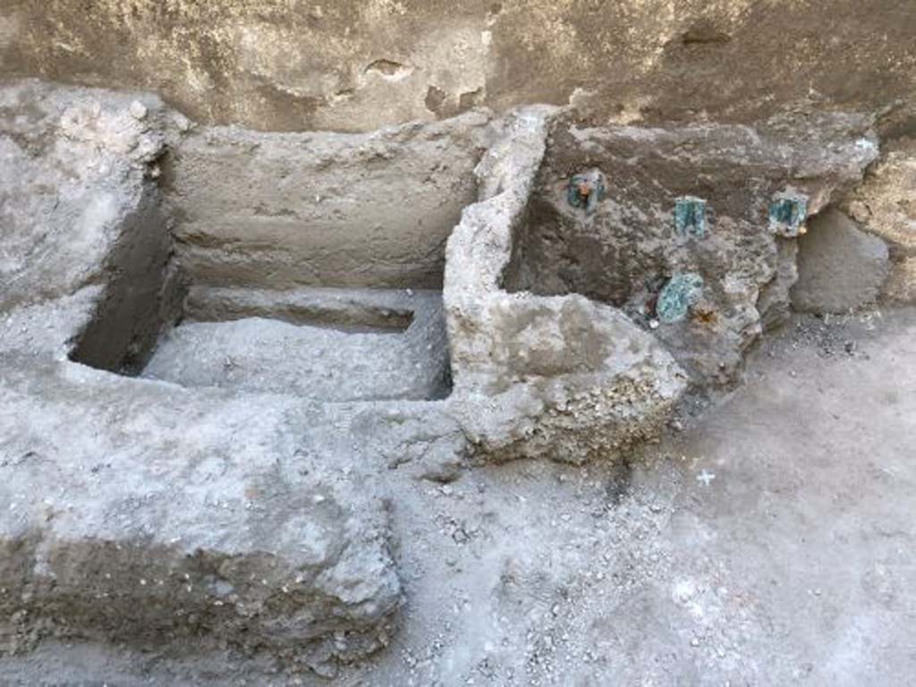 V.3 Pompeii. Casa del Giardino. August 2019. Outline of the wooden box which contained the gems.
Kept in a wooden case, and recently restored and brought to their former glory by the restorers of the Restoration Laboratory of the Archaeological Park of Pompeii, they formed part of the precious valuables of the family, which perhaps the inhabitants of the house could not take away before attempt ing to escape. The trace of the wooden case that contained the finds, whose bronze hinges have been well preserved inside the volcanic material, unlike the wooden decomposed part, was identified next to the imprint of another case or piece of furniture in the corner of one of the service areas, probably used as a repository.

Impressione della cassa di legno che conteneva le gemme.
Custoditi in una cassa in legno, e da poco restaurati e riportati al loro splendore dalle restauratrici del Laboratorio di Restauro del Parco Archeologico di Pompei, si trattava di una parte dei preziosi di famiglia, che forse gli abitanti della casa non riuscirono a portare via prima di tentare la fuga. La traccia della cassa in legno che conteneva i reperti, le cui cerniere bronzee si sono ben conservate all’interno del materiale vulcanico, a differenza della parte lignea decompostasi, è stata individuata accanto all’impronta di un’altra cassa o mobile nell’angolo di uno degli ambienti di servizio, probabilmente usato come deposito.

Photograph © Parco Archeologico di Pompei.

