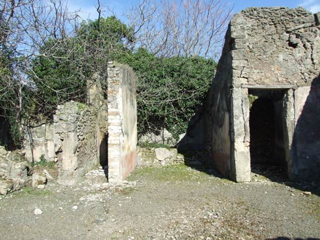 V.4.c Pompeii. March 2009. Room B, the atrium, looking east. Looking across atrium to doorways to room F, on left, room J, corridor to garden, room G, tablinum, and room H, cubiculum.  When excavated the atrium had flooring similar to that of the fauces, opus signinum/cocciopesto.
V.4.c Pompeii (described as second house after that of Lucrezio Frontone).
Found on 15th March 1902, between the upper layers of a room near the tablinum, was an oxidised statuette (100mm high) of a bearded and crowned Hercules, leaning with the weight of his body on his right leg, since the left leg was slightly bent. In his right hand he held the club pointing downwards, and in his left hand he held the apples of the Hesperides; the lions skin was hanging on his left forearm. If he was beardless, he would have very closely resembled the Hercules Righetti of the Vatican Rotunda. Also found were  a bronze cylindrical bell with an iron ringer/clapper. An oxidised medium and small bronze coin. A glass bottle with a spherical belly. Found on the 24th March in the same place was a terracotta single-burner lamp, with a ring handle. See Notizie degli Scavi di Antichit, 1902, (p.213)

