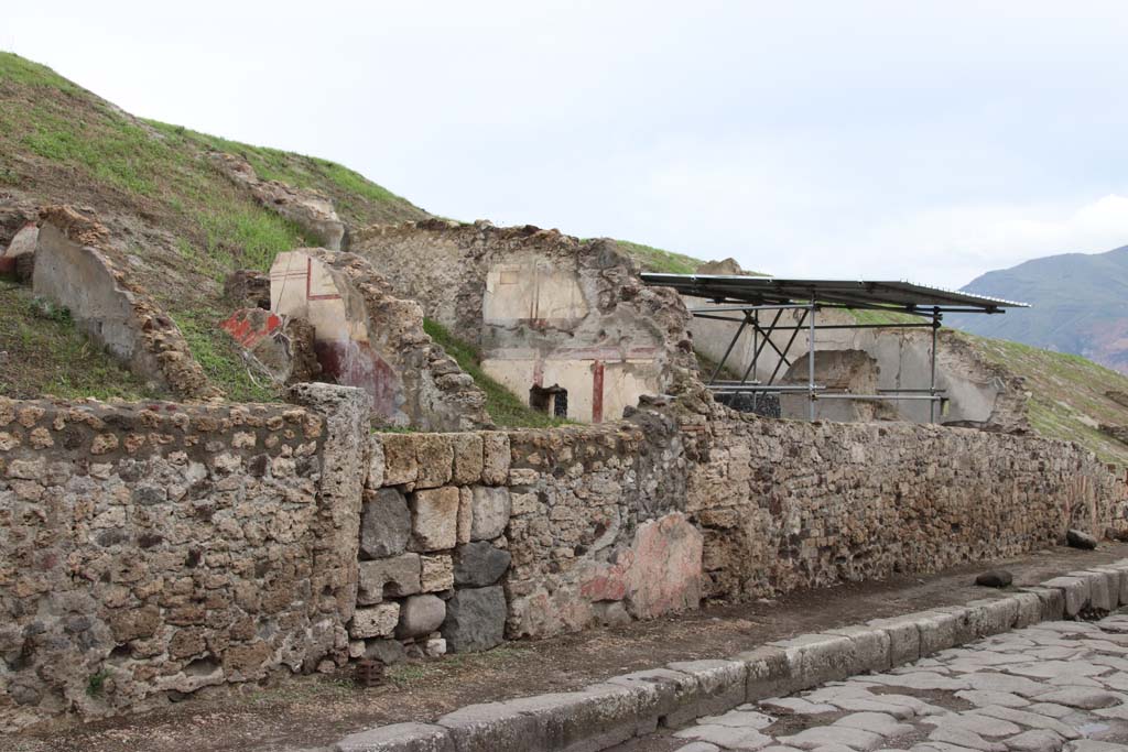 V.6.7 or 8 Pompeii, Pompeii. October 2020. Looking south along east side of Via del Vesuvio. Photo courtesy of Klaus Heese.
(Note: the roofed area where the lararium is seen above the wall, originally we had identified as V.6.7.
According to Massimo Osanna's book the lararium area is shown as casa 4 and the three front rooms to the north (left) is casa 3.
There does not seem to be a doorway entering the lararium area from this roadway or casa 3, so perhaps the numbered entrance doorway would be further at the rear, still buried. 
Therefore, perhaps the doorway with the large blocks in centre left, is now V.6.7.)
See Osanna M., 2019. Pompei. Il tempo ritrovato. Le nuove scoperte. Milano: Rizzoli, p. 216, fig. 4.