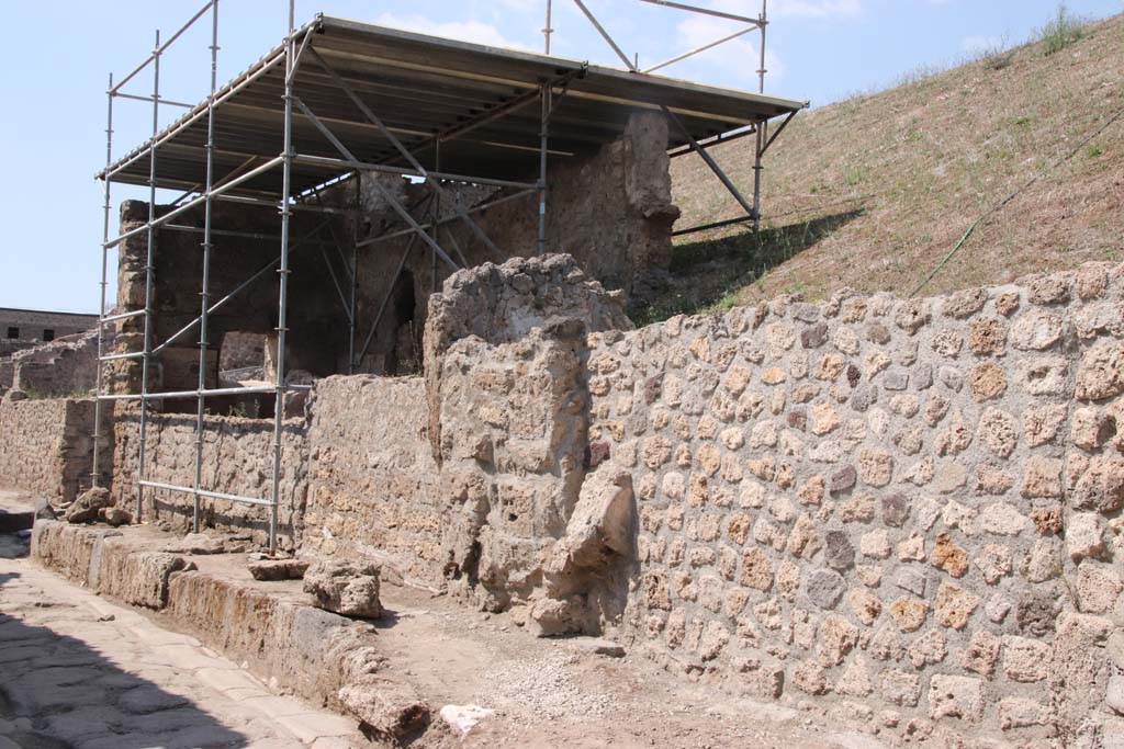 V.7.1 Pompeii, centre left, under roof, on north side of Vicolo delle Nozze d’Argento. September 2021. 
Looking west along front of insula, towards junction with partly newly excavated roadway, on left. Photo courtesy of Klaus Heese.
