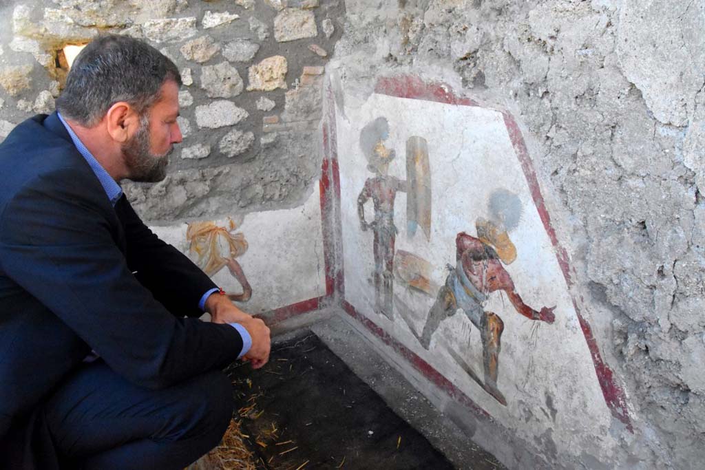 Massimo Osanna studies the fresco of two gladiators at the end of the fight, one wins the other succumbs.  
It is the scene of the latest fresco found in Pompeii in Regio V, as part of the work of securing and remodulating the excavation fronts, provided for by the Great Pompeii Project. It is the scene of a fight between a "Mirmillo" and a "Thracian", two types of fighters distinct from different armour and classic opponents in gladiatorial fights. The discovery environment is only partially brought to light - on one side emerges another small portion of fresco that reveals the presence of another figure.

Massimo Osanna studia l'affresco di due gladiatori al termine del combattimento, l’uno vince l’altro soccombe. E’ la scena dell’ultimo affresco rinvenuto a Pompei nell’area di cantiere della Regio V, nell’ambito dei lavori di messa in sicurezza e rimodulazione dei fronti di scavo, previsti dal Grande Progetto Pompei. Si tratta della scena di un combattimento tra un “Mirmillone” e un “Trace”, due tipologie di lottatori distinti da armature differenti e classici avversari nelle lotte gladiatorie.
L’ambiente di rinvenimento è solo parzialmente portato in luce - su un lato emerge un'altra piccola porzione di affresco che rivela la presenza di un’altra figura.

Photograph © Parco Archeologico di Pompei.
