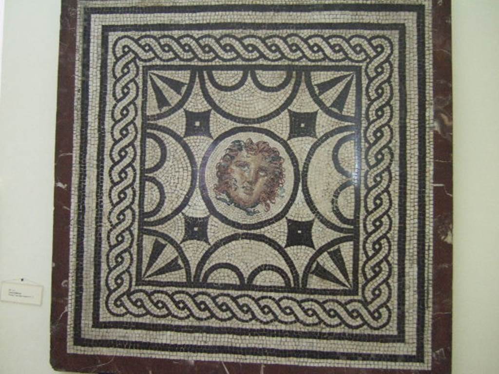 Found in VI.1.7 Pompeii. Mosaic with head of Medusa. 
Now in Naples Archaeological Museum. Inventory number s. n.
According to Pagano and Prisciandaro –
11 Novembre 1784, Cubicolo – 
“Si continua a scavare nella consaputa abitazione, e si e scoperta una stanza. Questa tiene il pavimento di musaico bianco, ed il piano suo vien distinto da un grado alto on.6. Tale altezza e ornata da un fascia di marmo, ed il detto piano superiore e di musaico liscio. E nel piano sottoposto vi e un quadro con dei lavori di musaico nero, e nel centro vi e una testa bellissima di Medusa anche di musaico. Le mura di questa stanza sono cosi dipinte: lo zoccolo giallo con alcuni lavori, il dippiu bianco con riquadrature di fasce rosse con varie pitture, festoni ed altro. Vi si e trovato – Bronzo: Una lucerna ad un luminello e suo manico. Un piccolo anelletto. Due chiodi ed una centrella. Osso: Un netta orecchie.”
See Pagano, M. and Prisciandaro, R., 2006. Studio sulle provenienze degli oggetti rinvenuti negli scavi borbonici del regno di Napoli. Naples: Nicola Longobardi.  (p.82 and see PAH,1,2,24 and Addendum p.40 (Il mosaico fu tagliato il 13 Decembre 1787).
(translation – 11th November 1784, Cubiculum –
"We continued to dig in the known house and found a room.  
This room had a white mosaic floor, and the floor was distinguished by a high step of 0.13m (approx. 5 inches high). 
This height was decorated by a strip of marble, and the said upper part of the floor was of smooth mosaic.  
And in the floor below, there was a picture worked with black mosaic, and in the middle there was a beautiful head of Medusa, also in mosaic. 
The walls of this room were painted: with a yellow zoccolo, with panels separated by red bands with various paintings, garlands and more. 
Bronze and bone items were found."
(Addendum: the mosaic was cut and taken to the Museum on 13th December 1787). (see below – sent on 21st December 1787).

PAH, 1787, p.40 –
13th Decembre 1787.
Si e mandato ad avvisare a Canart, che mandi a tagliere li due quadri di musaico, secondo ordino il sig. Ajutante D. Pietro La Vega. 
Uno e quello con la testa di Medusa di pal 3 ed on.8 in quadro; l’altro e quello con lo scheletro, che tiene in ciascuna mano, un vaso con la bocca inclinata verso la terra, di pal. 2 ¾ per pal. 2 ed on.5.
21st Decembre 1787.
Si sono mandati questa mattina pel R. Museo a D. Giuseppe Canart i due quadri di musaico, notati nel passato rapporto.
(translation - 13th December 1787.
One has sent to advise Canart to cut the two mosaics, according to the orders of La Vega.  One is the one with the head of Medusa of 0.97m squared;  
the other that with the skeleton holding a vase in each hand with the mouth tilted towards the earth, 0.73m x 0.64m. 
21st December 1787.
This morning, one has sent the two squares of mosaics, noted in the past report to the Royal Museum to D. Giuseppe Canart.)
(Note – the mosaic of the skeleton with the vase in each hand was excavated from VI. Ins. Occ. 25).

