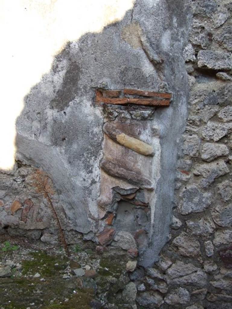 VII.15.13 Pompeii. December 2007. Lararium in kitchen area. According to Boyce, in the kitchen, located on the east side of the entrance fauces on the east wall above the hearth, was the lararium. An altar in the form of a low half-column of stucco was applied to the wall and painted red.
Around it coiled a serpent in yellow stucco relief, half of its body in elaborate rings above and to the right of the altar, and actually tied into a knot. Above the top of the altar “the usual fruits” were reported to have been painted. On each side was the figure of a Lar. The whole painting was bordered by red stripes, and across the top were stretched three garlands.
See Boyce G. K., 1937. Corpus of the Lararia of Pompeii. Rome: MAAR 14.(p.73, no.335, and Pl.23,2) 

