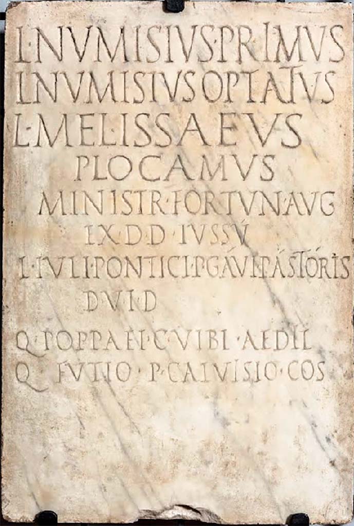 VIII.1.1 Pompeii. 
Dedicatory inscription to Lucius Numisius Primus, Lucius Numisius Optatus, Lucius Melissaeus Plocamus, ministry of Fortuna Augusta.
Now in Naples Archaeological Museum. Inventory number 3771.

According to Cooley, this translates as –
Lucius Numisius Primus, Lucius Numisius Optatus, Lucius Melissaeus Plocamus, attendants of Augustan Fortune; in accordance with a decree of the town councillors, by command of Lucius Iulius Ponticus and Publius Gavius Pastor, duumvirs with judicial power, and of Quintus Poppaeus and Gaius Vibius, aediles, in the consulship of Quintus Futius and Publius Calvisius. (CIL X 827 = ILS 6384)
See Cooley, A. and M.G.L., 2014. Pompeii and Herculaneum: A Sourcebook. London: Routledge, p. 136, E50.

According to Epigraphik-Datenbank Clauss/Slaby (See www.manfredclauss.de) this reads

L(ucius) Numisius Primus
L(ucius) Numisius Optatus
L(ucius) Melissaeus
Plocamus
ministr(i) Fortun(ae) Aug(ustae)
ex d(ecreto) d(ecurionum) iussu
L(uci) Iuli Pontici P(ubli) Gavi Pastoris
d(uum)v(irorum) i(ure) d(icundo)
Q(uinti) Poppaei C(ai) Vibi aedil(ium)
Q(uinto) Futio P(ublio) Calvisio co(n)s(ulibus)      [CIL X 827]


