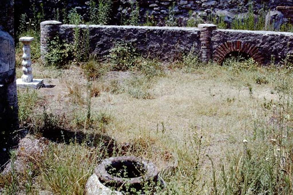 VIII.4.12 Pompeii, 1968. Looking west across portico.  Photo by Stanley A. Jashemski.
Source: The Wilhelmina and Stanley A. Jashemski archive in the University of Maryland Library, Special Collections (See collection page) and made available under the Creative Commons Attribution-Non-Commercial License v.4. See Licence and use details.
J68f1200
According to Wilhelmina, this was a shop-house, with the garden (excavated in 1861) at the rear at the back of two shops (VIII.4.12 and 13).
The garden had a portico on four sides. Seven huge dolia were buried in the soil along the edge of the east half of the garden.
In the south-west corner there was a masonry pool with a little column in the middle, which jetted water. A marble monopodium was also found.
On the right side of the peristyle there was a bronze basin (0.40m in diam.) with a hole in the middle through which a small pipe entered.
On the pipe was a little lion which jetted water from its mouth and throat. The feet of the basin were welded in the form of a ring.
The fragment of a head of a statuette was also found on the right side of the peristyle.
See Jashemski, W. F., 1993. The Gardens of Pompeii, Volume II: Appendices. New York: Caratzas. (p.213).

