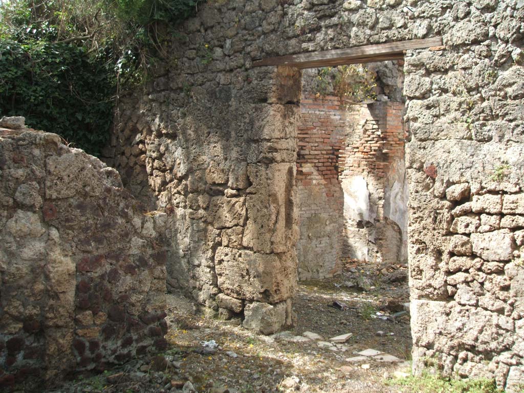 IX.7.19 Pompeii. May 2005. 
Looking south-west from room g, towards doorway in south wall into room h, and in west wall leading into room b, the atrium, on right.
According to Mau, the best conserved parts of the floor in room g, showed that the couches were for at least twelve persons. 
They had leaned against the rear wall, and against the rear right and rear left wall.
The decoration was the same as in the atrium, also with a white background, but simpler and without paintings. 
The door closed from the internal part by half a beam, inserted in two holes in the doorpost, the one on the right a little higher than the other.
The doorway in the south wall, on the left, leads into room h, a cubiculum.
According to Mau, the cubiculum was not accessible other than from room g.
In this doorway there was no trace of either a threshold or hinges, and it seemed that the doorway had always remained open.
In the east wall, there was a small square window with an impression of a wooden window-frame. 
The decoration, on white background and of the same style as that of rooms b and g, contained the following –
Left (west) wall – (size: conserved height 1.0m x conserved length 0.64m) country scene on a white background, showing a rural shrine shaded by a sacred tree, surrounded by a yellow balustrade with a broken herm of Priapus and a thyrsus, leaning against it. There were also two other unknown figures 
Entrance (north) wall near the door, pendant to no.1. (size: height I.15m x length 0.76m) the other country scene showed the usual shrine shaded by a tree and in front of this above a pedestal was an image in bronze of a crowned Hercules, with his lion skin and his club on his left arm, and drinking cup in his outstretched right hand. In front of the image stood a man and a burning altar. At the back, there was a bridge with two goats on it.
Entrance (north) wall, to the right of no.2: fragment, (size: height 0.11m x length 0.44m) – Fishes and shells.
Left side of left (west) wall (size: height 0.175m x length 0.325) – A bird with some cherries, and above a shelf some other fruits, but only two were visible on the left, perhaps apples? (The rear part of the painting had vanished). 
Right side of left (west) wall, pendant to no.4, (hardly conserved), fruit in two places, at least another fruit but not distinguishable.
See Mau, Bullettino dell’Instituto di Corrispondenza Archeologica (DAIR), 1883, (p.80-81).

According to Sogliano in NdS, the paintings found in room h, were in the most part destroyed when excavated. Two country scenes remained, one on the west wall which was damaged on the left side of it – see no.1 above, and the other country scene on the extreme west of the north wall  - see no.2 above.
See Notizie degli Scavi di Antichità, 1880, (p.491).
