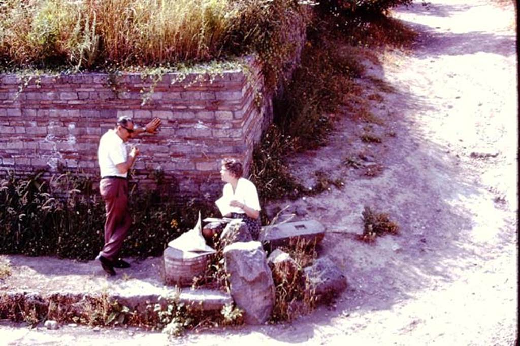 Vicolo dell’Anfiteatro, Pompeii. 1976. Looking south towards east side, with Wilhelmina resting in the shade, and talking to Sig. Sicignano. Photo by Stanley A. Jashemski.   
Source: The Wilhelmina and Stanley A. Jashemski archive in the University of Maryland Library, Special Collections (See collection page) and made available under the Creative Commons Attribution-Non Commercial License v.4. See Licence and use details. J76f0314
