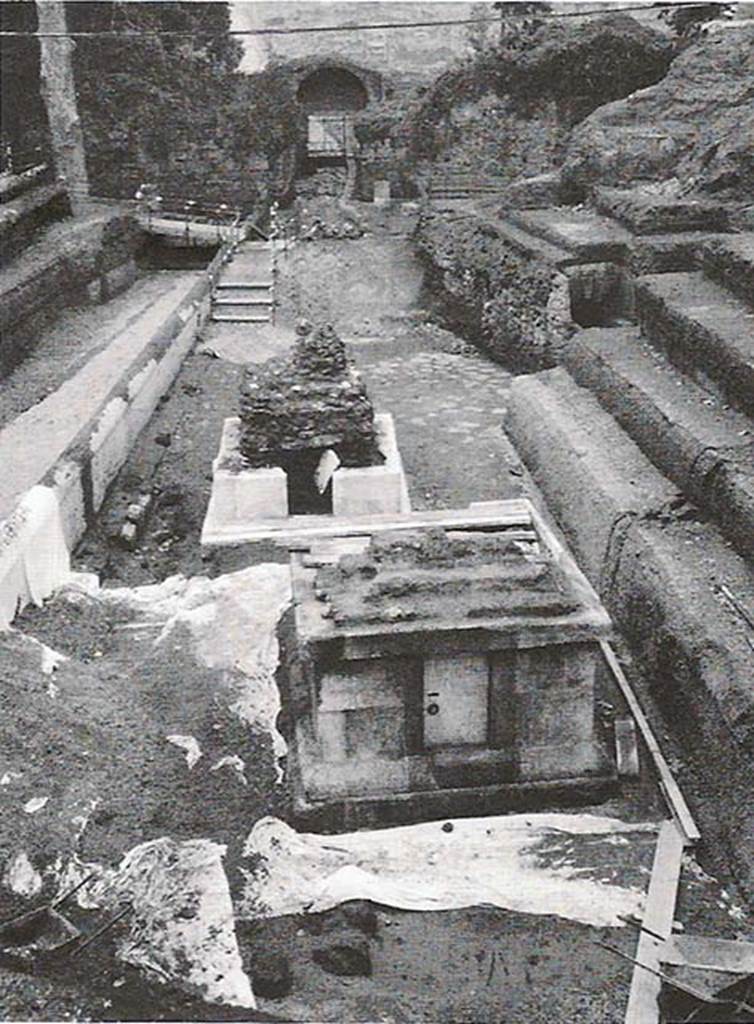 Tomb SG5 Pompeii. Looking north across SG5 and SG4 to the Porta Stabia.
According to Campbell, this is an altar type tomb, with a podium consisting of a substructure 0.18m high, a moulded base 0.35m high, two courses of large blocks 1.25m height and a projecting course of stone blocks 0.28m high all of limestone.
Travertine facing (0.16m) was still in situ on the north and east sides.
Evidence of two steps and part of core of tufa on the south side suggest an altar superstructure.
The interior of the tomb is a single room with vaulted ceiling, cocciopesto floor and some traces of white painted stucco.
Three of the walls contain two rectangular niches each, and all but one held glass cinerary urns containing burnt bones.
The door is in the fourth, south, wall. Graffiti was found on the door.
A clay lamp and seven glass ointment jars were found in the tomb, dating it stylistically to the 1st century AD.
The construction method dates it to mid to late 1st century.
See Campbell V.L., 2014. The Tombs of Pompeii: Organization, Space, and Society. Routledge: Abingdon UK, p. 304-5. 
On the left is a wall in opus incertum.
See D’Ambrosio A., 2001-2. Rivista di Studi Pompeiani XII-XIII, p. 220, fig. 1
See D’Ambrosio A., 2003. Rivista di Studi Pompeiani XIV, p. 287.
